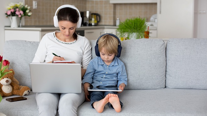 woman working from home wearing headphones with young child